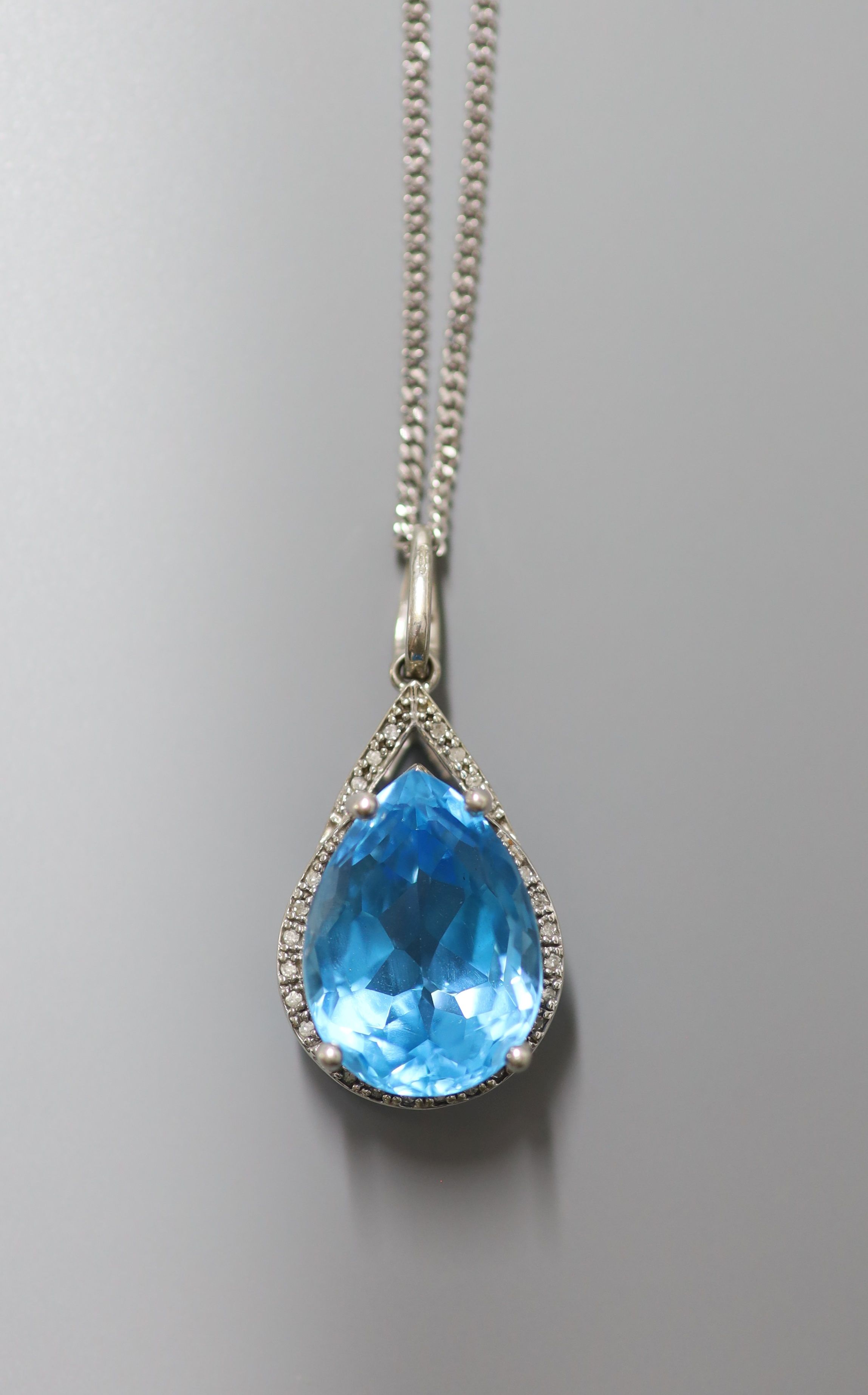 A modern white metal (stamped 9k), blue topaz and diamond chip set pendant, 29mm, on a 9ct white gold chain, 44cm, gross weight 12.3 grams
